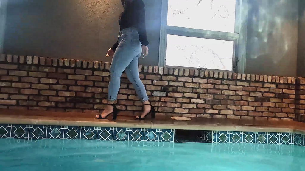 Reyna springt im Jeans und glänzenden schwarzen Oberteil in den Pool