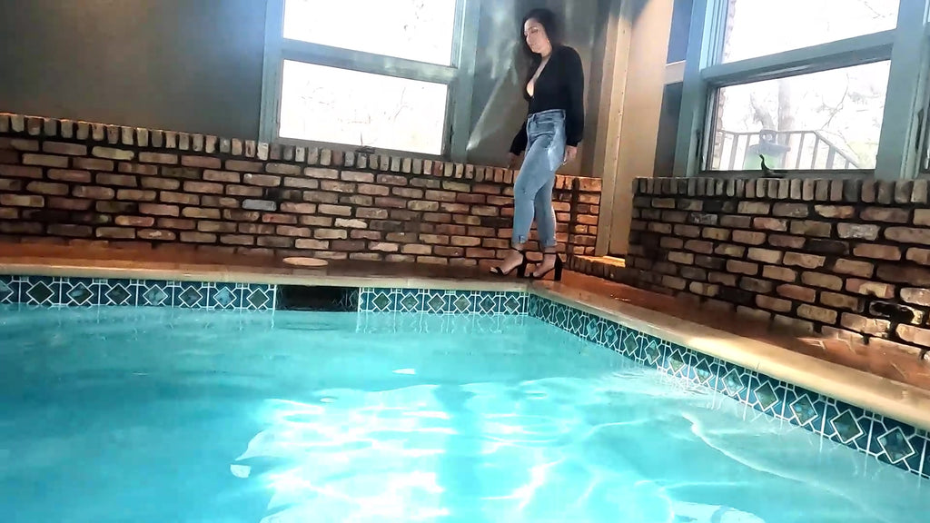 Reyna springt im Jeans und glänzenden schwarzen Oberteil in den Pool