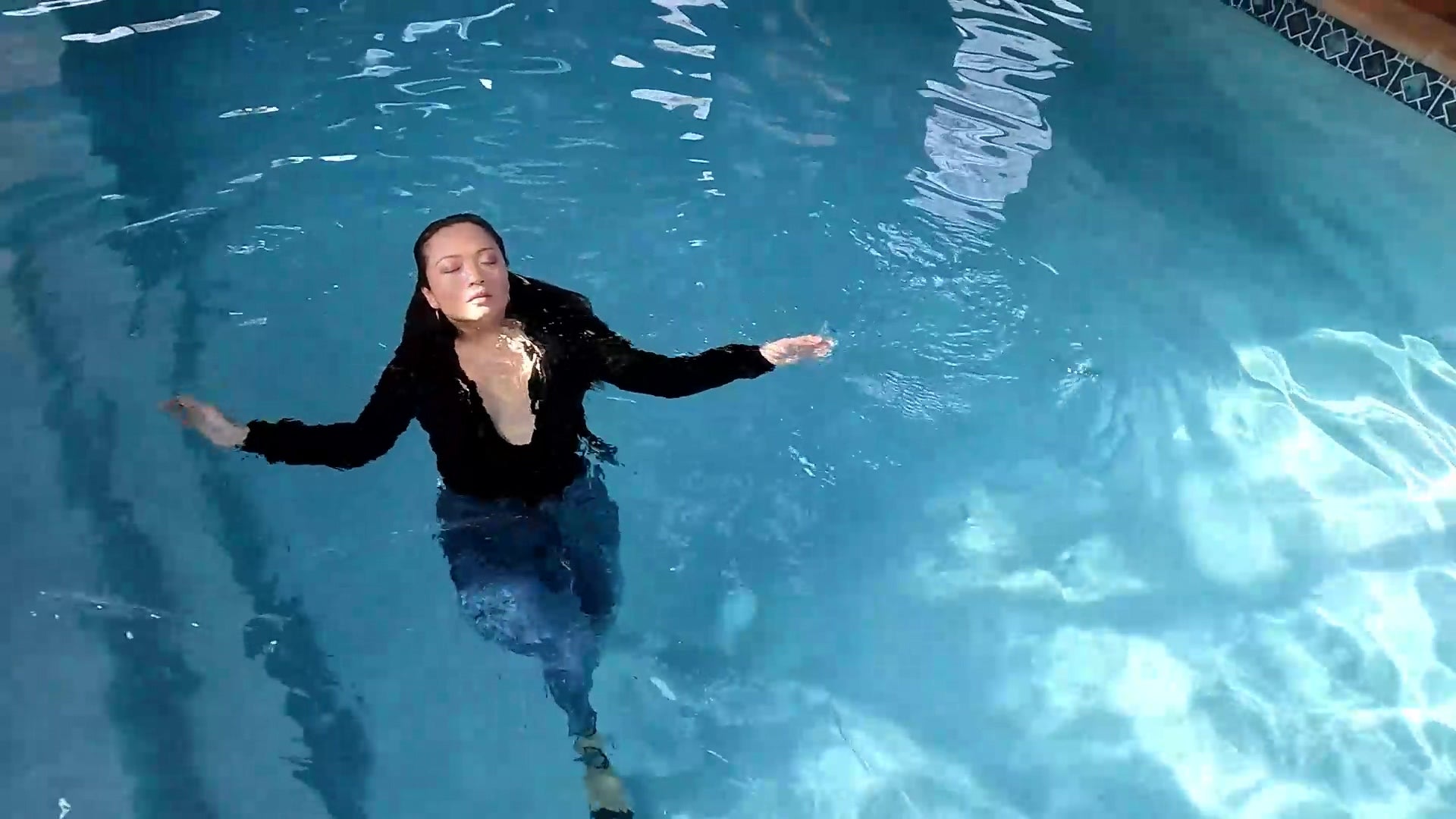 Reyna springt im Jeans und glänzenden schwarzen Oberteil in den Pool