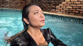 Reyna springt im Jeans und glänzenden schwarzen Oberteil in den Pool